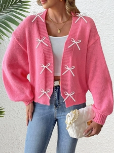 Close-up of pink knit cardigan featuring decorative white bows and ribbed cuffs
