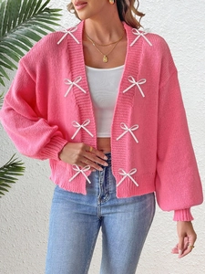 Close-up of pink knit cardigan featuring decorative white silk bows and ribbed cuffs