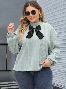 Detail of mint green ribbed long sleeve top featuring a large black bow and high neck