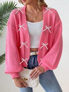 Detail of pink knitted cardigan with white bow accents and lantern sleeves on model