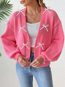 Detail of bright pink chunky knit cardigan featuring white ribbon bow embellishments