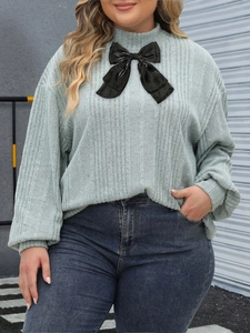 Close-up of a rib-knit long sleeve top featuring a contrast black velvet bow at the neckline