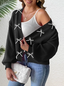 Detail of black knitted cardigan featuring 3D white ribbon bow accents and thick texture