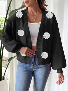 Women's black knit cardigan featuring oversized white 3D crochet flowers and ribbed cuffs