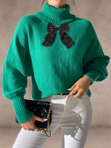 Detail of green knit sweater showing high turtleneck and large black satin bow decoration