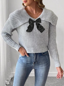 Gros plan sur un pull en maille grise avec un grand nœud noir et un large col revers