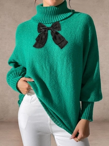 Close-up of green turtleneck sweater featuring a large black bow and chunky knit texture