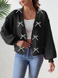 Detailed close-up of a black knit cardigan featuring white ribbon bow appliques on the front