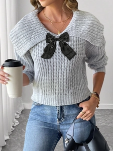 Détail du pull en maille grise avec col en V et accent de nœud en satin noir chic