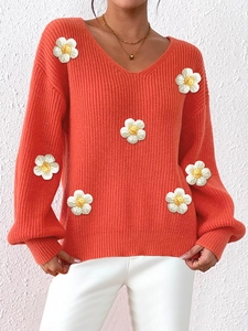 Detail of bright orange V-neck knit sweater featuring 3D white crochet flower patches