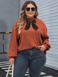 Detail of caramel ribbed knit top featuring a large black decorative ribbon bow at the neckline