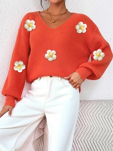 Detail of the 3D white knitted flowers on an orange V-neck textured sweater