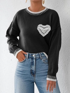 Detail of black knit sweater featuring white lace heart patch and striped cuffs