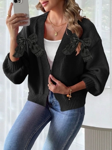 Detail of black cardigan featuring large satin bow accents on shoulders and knit texture