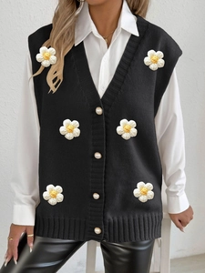 Detailed close-up of a black knit vest featuring 3D white daisy floral appliques and pearl buttons