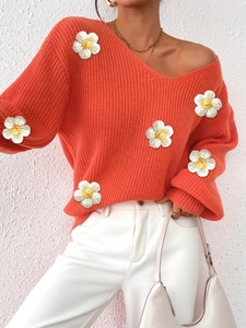 Detail of coral knit sweater featuring 3D white flower appliques and V-neckline texture