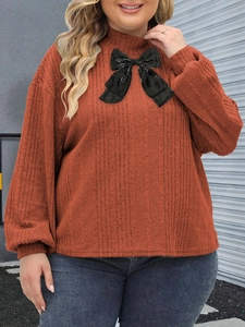 Detail of plus size orange ribbed knit top featuring a high neck and large black bow