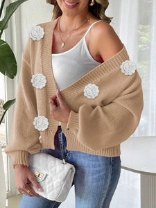 Close-up of beige knit cardigan featuring 3D white crochet flowers and textured fabric