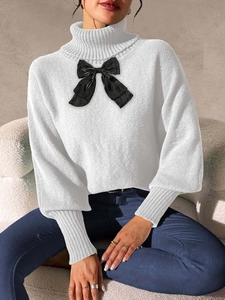 Close-up of a white high neck knit sweater featuring a large glossy black bow detail