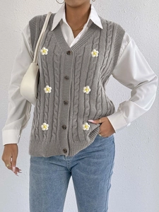 Detail of grey cable knit cardigan vest featuring 3D white daisy flowers and brown buttons