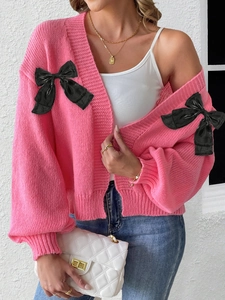 Detail of pink knitted cardigan featuring oversized black velvet bows and textured knit