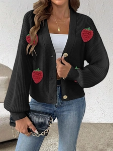 Dettaglio di un cardigan nero in maglia con graziose toppe a fragola rossa 3D e bottoni