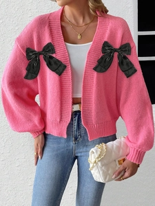 Detailed view of pink knitted cardigan featuring large black satin bows and V-neckline