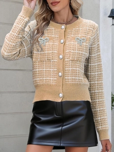 Detail der Strickjacke mit Perlenknöpfen und Strass-Schleifen auf khakifarbenem Karomuster