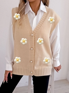Close-up of beige knit vest featuring elegant pearl buttons and 3D floral appliqués