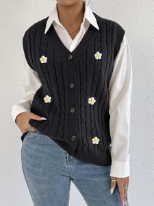 Close-up detail of knitted cable vest featuring 3D white floral appliqués and dark buttons