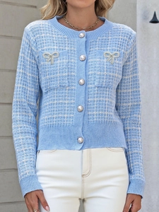 Detailansicht der Perlenknöpfe und glitzernden Schleifenbrosche auf blauer Strickjacke