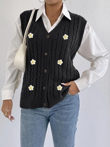 Close-up of black knit vest featuring 3D daisy patchwork and V-neck button design