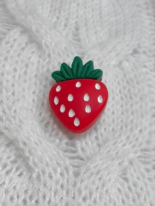 Detailed close-up of 3D strawberry button decoration on chunky cable knit fabric texture