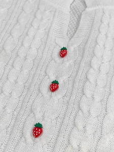 Close-up of white cable knit dress featuring vibrant red strawberry buttons decoration
