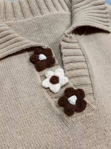 Detailed close-up of beige knitted polo collar with brown crochet flower decorations