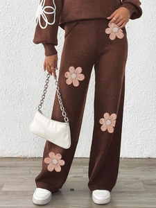 Detailed view of pink floral applique with white pearl beads on brown knitted fabric