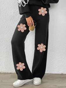 Detail of black knit wide-leg trousers featuring 3D pink floral patches with bead centers