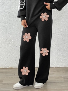 Close-up of pink floral 3D embroidery and knit texture on black wide leg trousers
