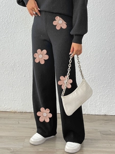 Detail of 3D floral appliques and beaded texture on black knitted wide leg trousers