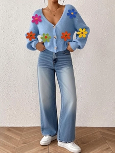 Détail des fleurs au crochet colorées en 3D sur le cardigan en maille bleu clair doux