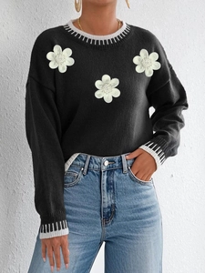 Close-up of black sweater featuring 3D floral embroidery and striped knit cuffs