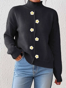 Detalle del tejido de un jersey negro de cuello alto con seis adornos de margaritas blancas