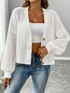 Detail of white knit cardigan with golden round buttons and textured openwork pattern