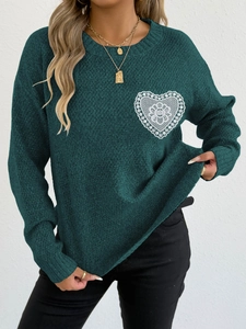 Detalle de un jersey de punto verde oscuro con un aplique de encaje blanco en forma de corazón