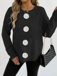 Détail d'appliqués de camélias blancs sur un pull en maille noire à manches longues