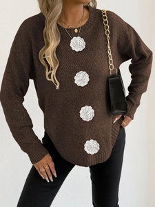 Détail d'élégantes fleurs 3D blanches sur un pull en maille marron foncé à manches longues