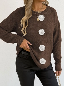 Détail des fleurs au crochet 3D blanches sur un pull en maille marron foncé à manches