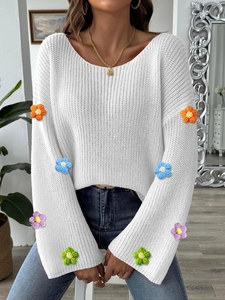 Detail eines weißen Strickpullovers mit bunten Häkelblumen an den Glockenärmeln