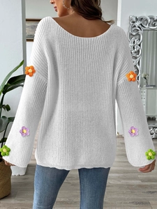 Detail der Strickstruktur des weißen Oversize-Pullovers mit bunten Häkelblumen an den Ärmeln