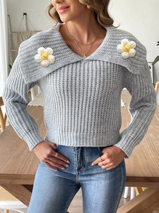 Detailed view of grey chunky knit sweater with large V-neck lapel and white crochet daisies